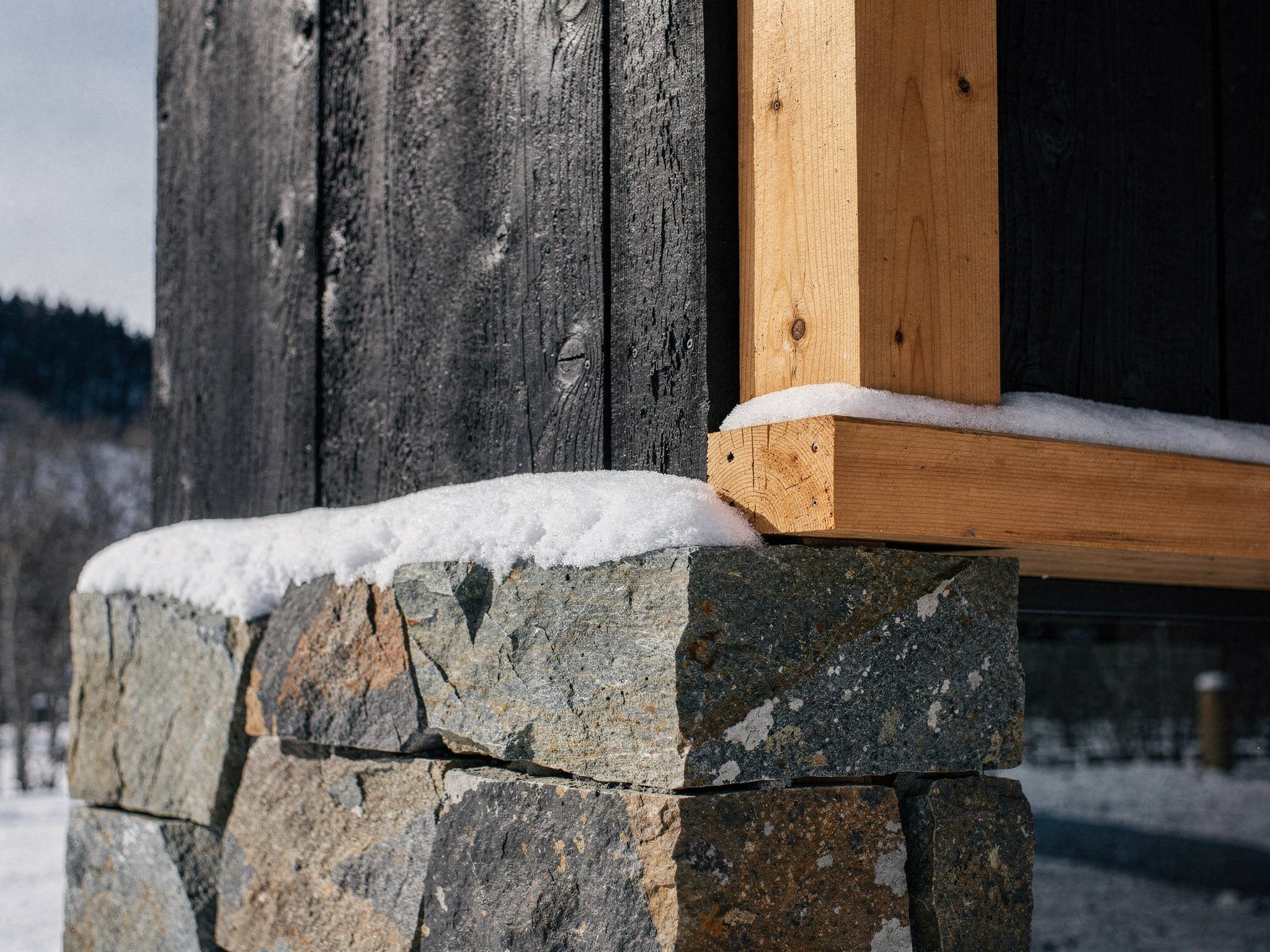 Junction of charred cedar, honey glulam and andesite stone with snow on the char