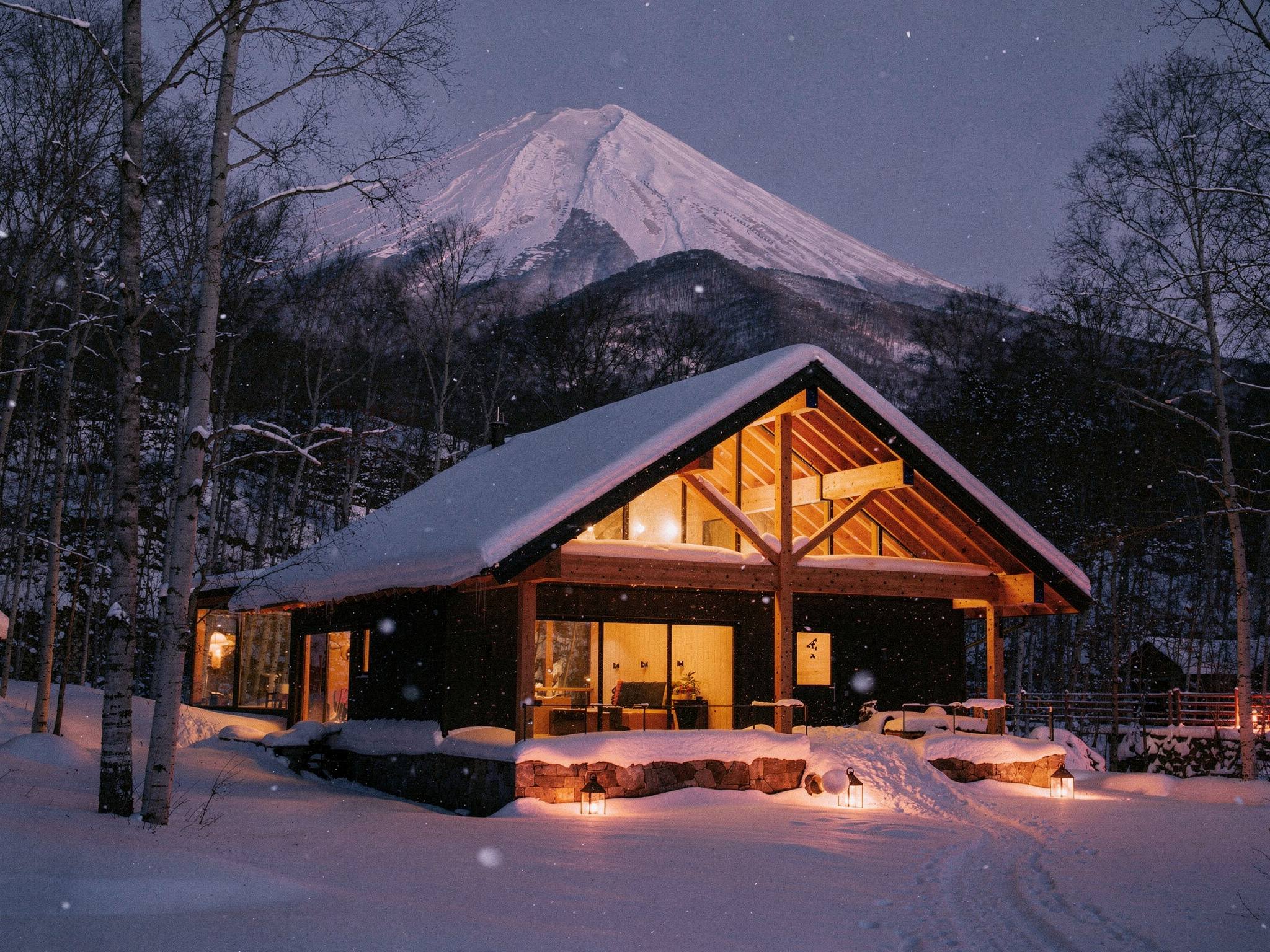 Lodge glowing warm at winter twilight, lantern path, Mt Yōtei behind