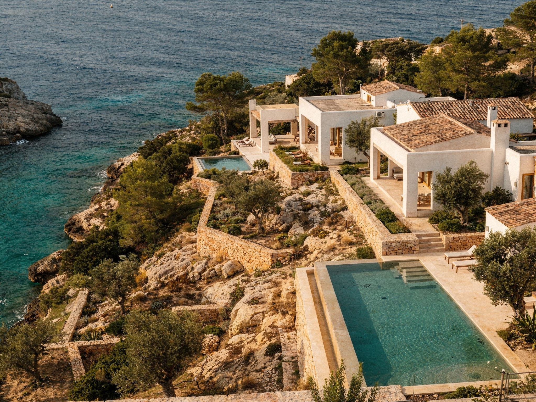 Aerial of the whitewashed villas stepping down the pine slope to a turquoise cove