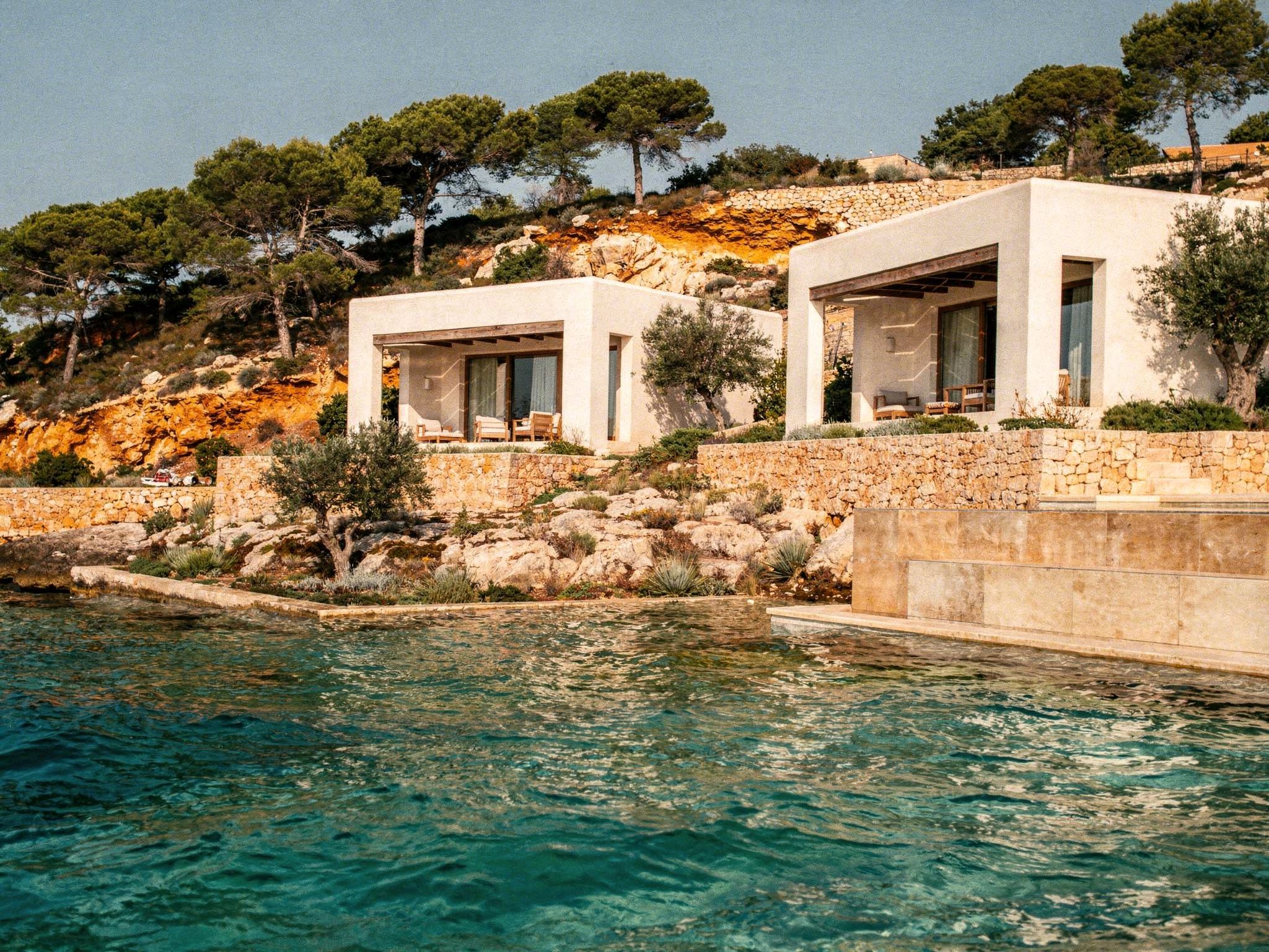 The villas seen from the water, whitewashed walls above golden cove rocks