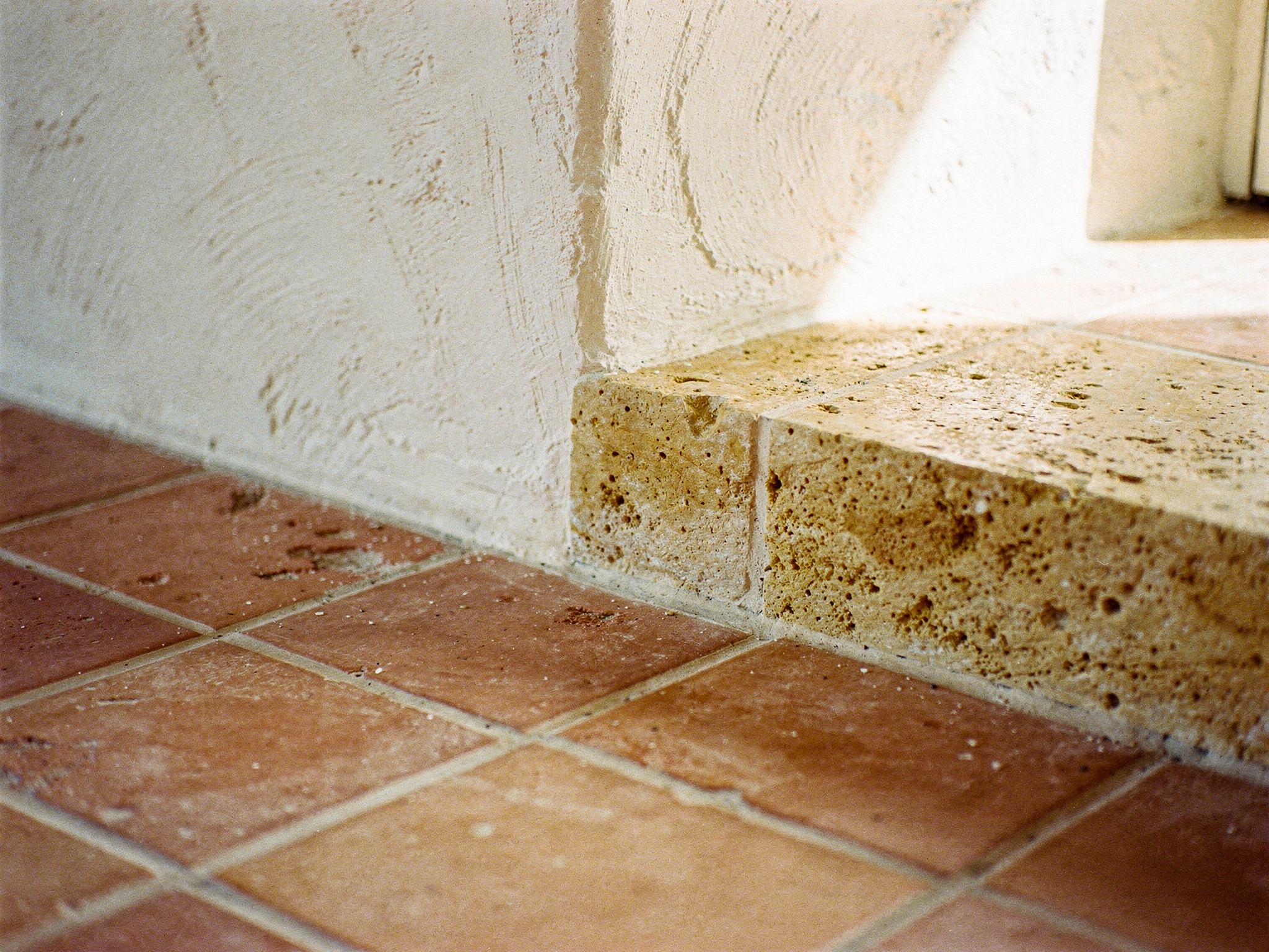 Terracotta floor tiles meeting a lime-plaster wall and a stone step