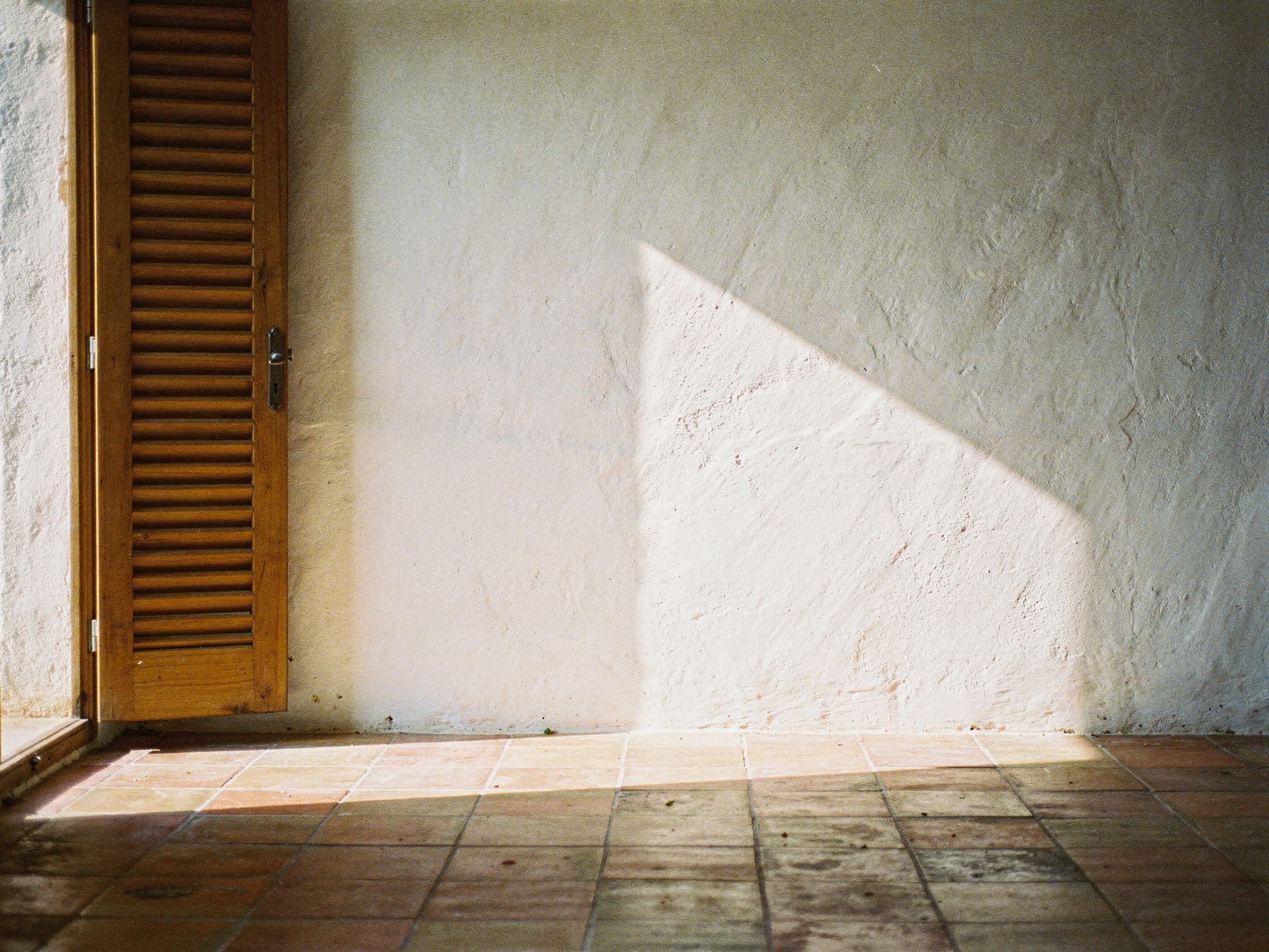 Shutter light falling across a whitewashed plaster wall and terracotta floor