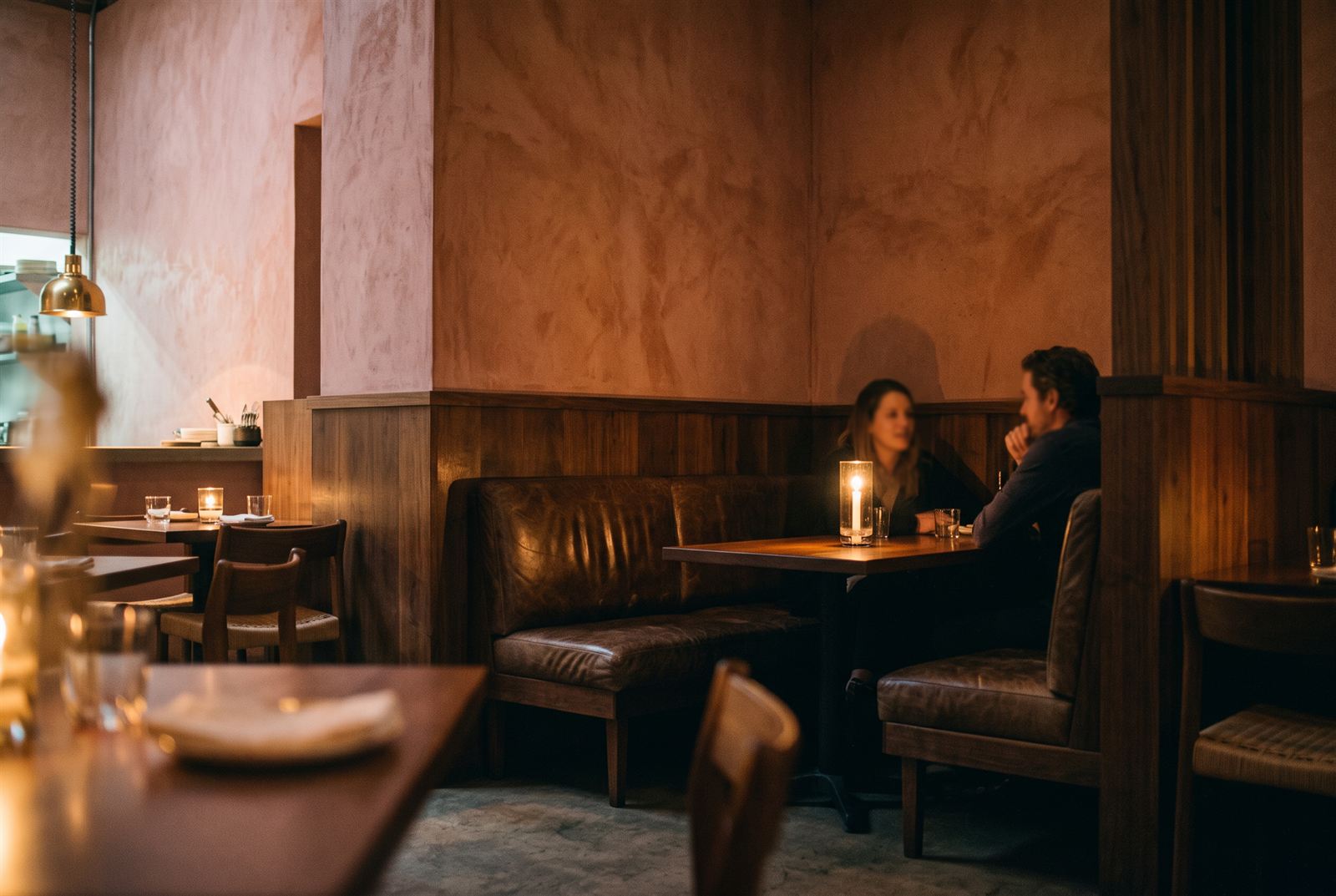 Corner banquette in worn leather and walnut panelling, a couple talking by candlelight