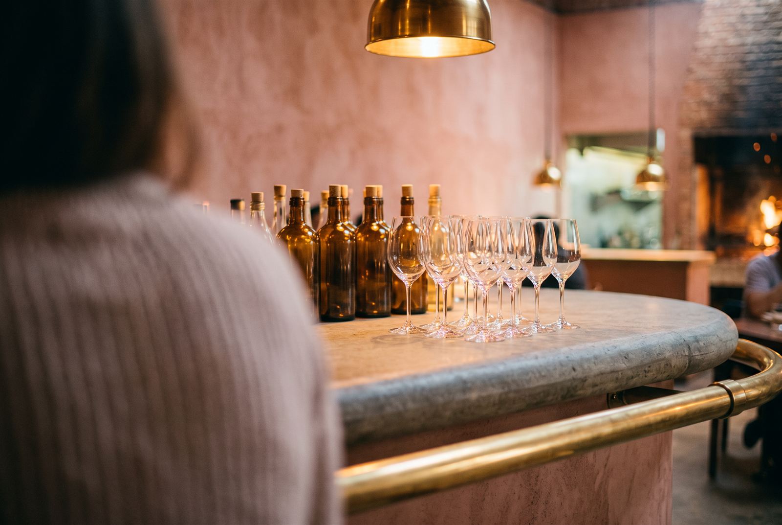 Bar detail — amber bottles and rows of stemware on the stone counter with its brass rail, the fire out of focus beyond