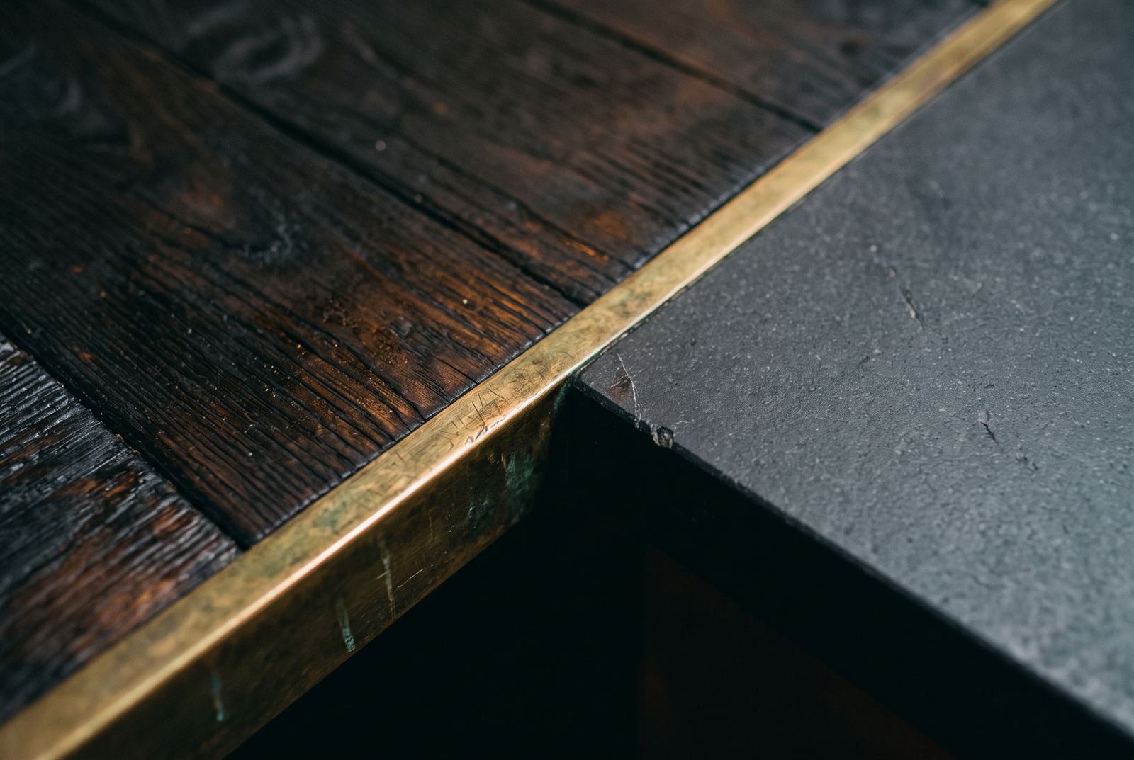 Materials detail — charred-oak boards meeting honed bluestone along a patinated brass edge trim