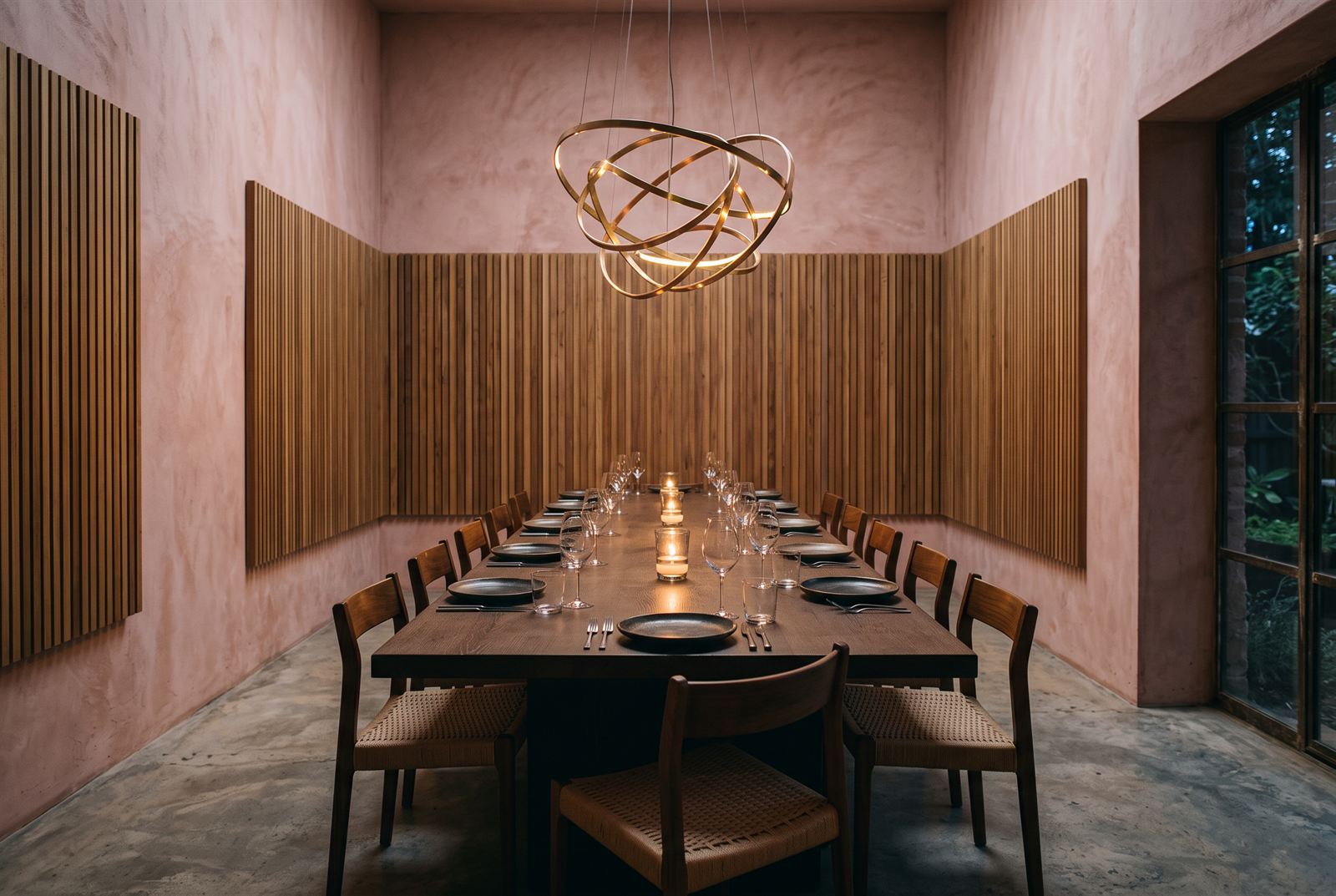 Private dining room — timber batten walls, a long dark-oak table set in black stoneware, a ringed brass chandelier above