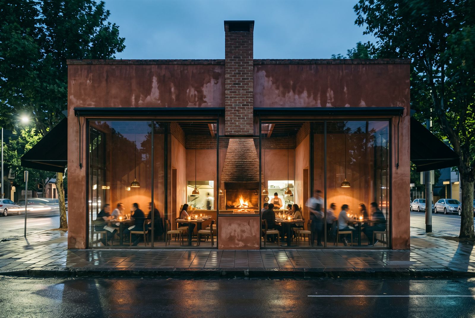 Dusk exterior — the brick chimney splitting the fully glazed facade, every table lit and the fire at the centre of the room