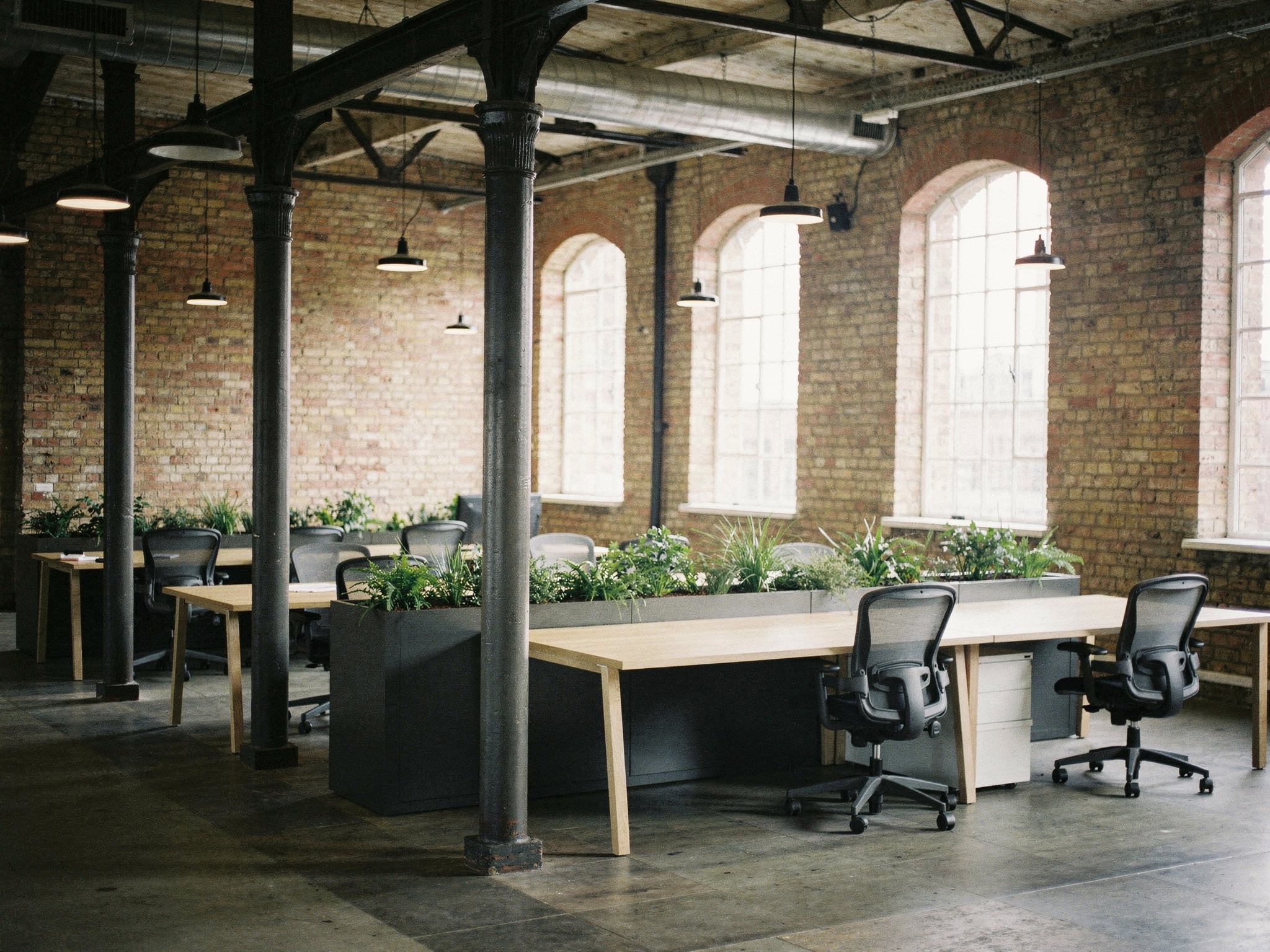 An open-plan office floor with brick, oak desks and tall arched windows