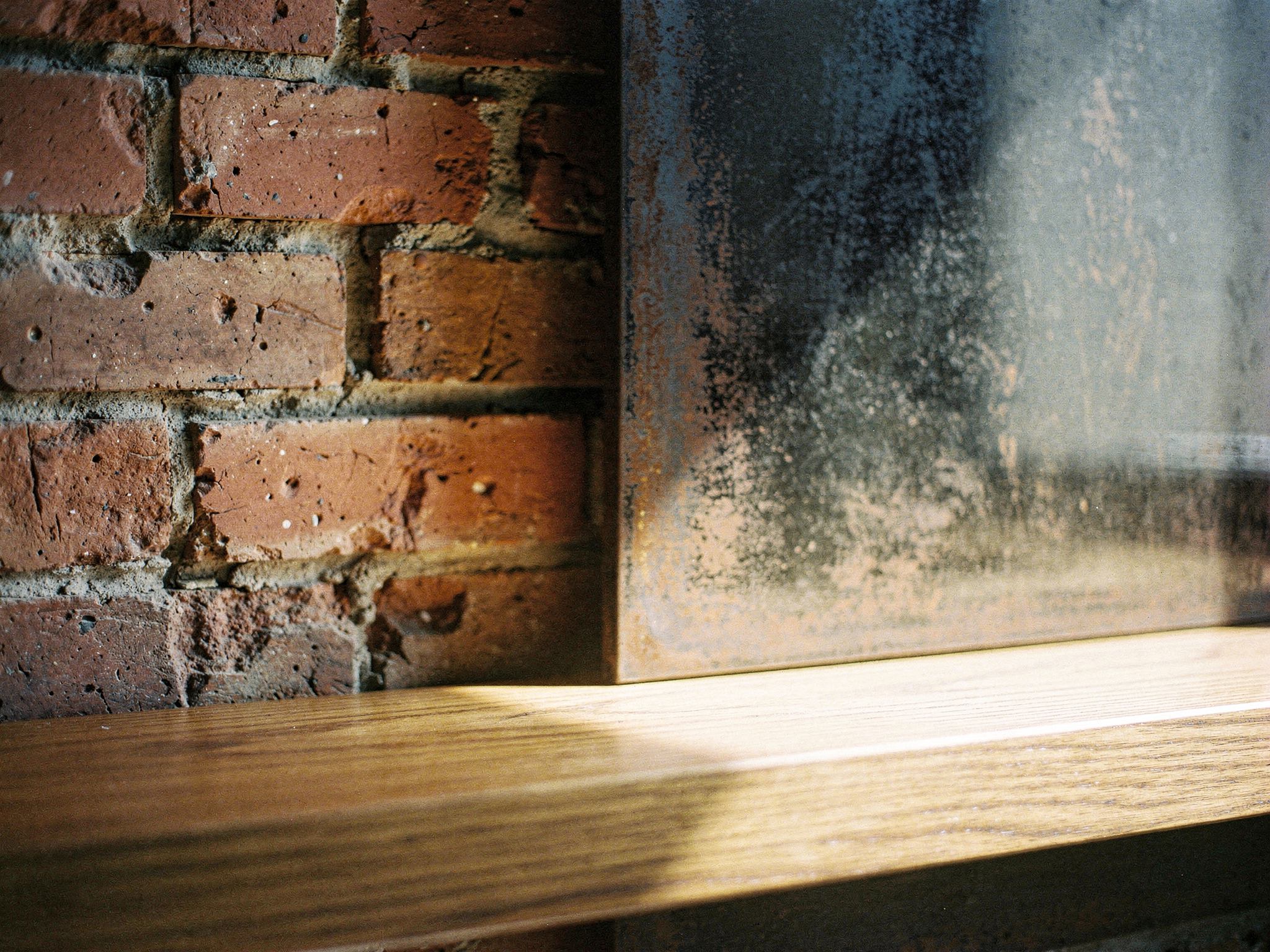 Weathered brick meeting a blackened-steel plate and oak sill