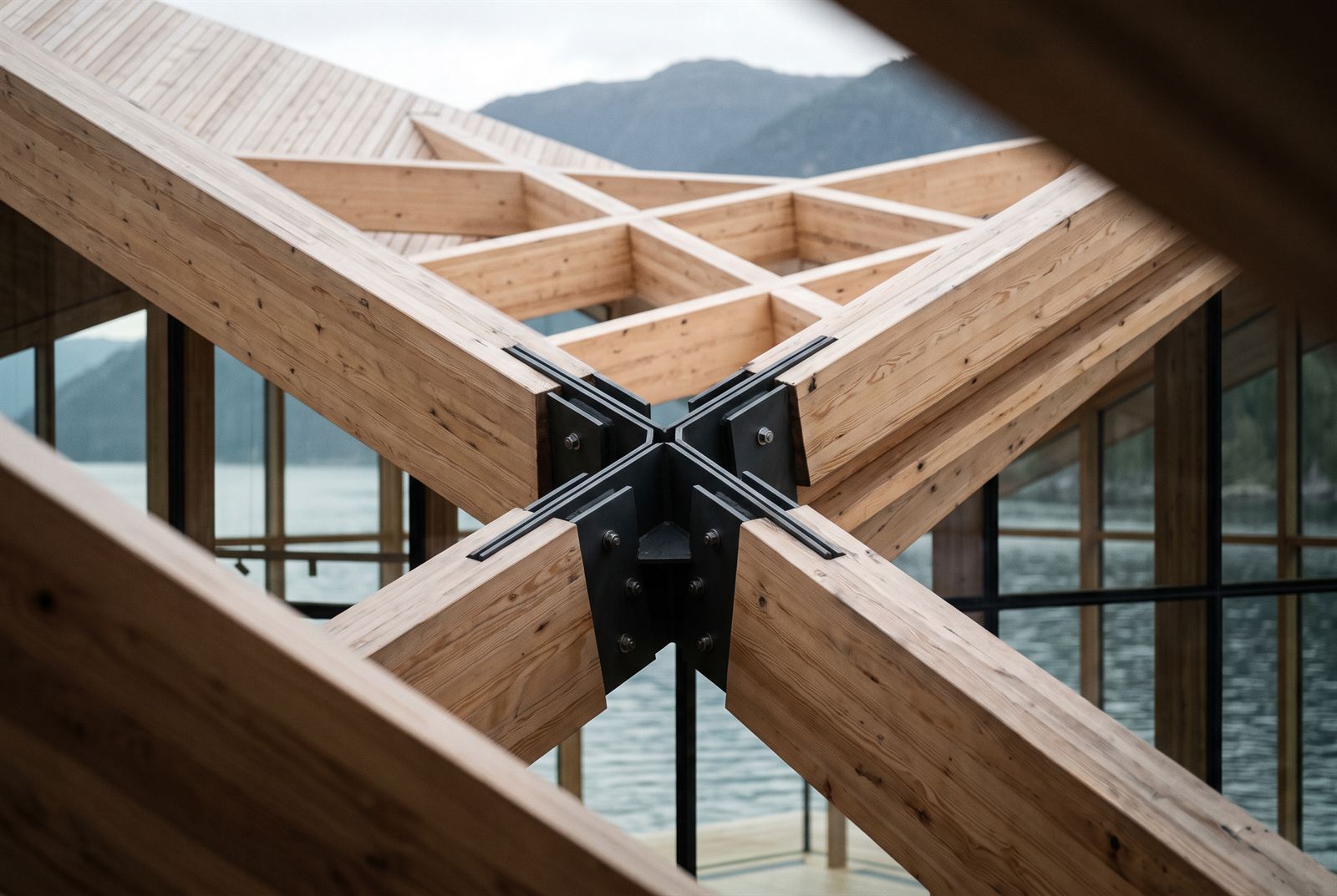 Close view of four glulam beams meeting in a blackened-steel node where the roof folds cross