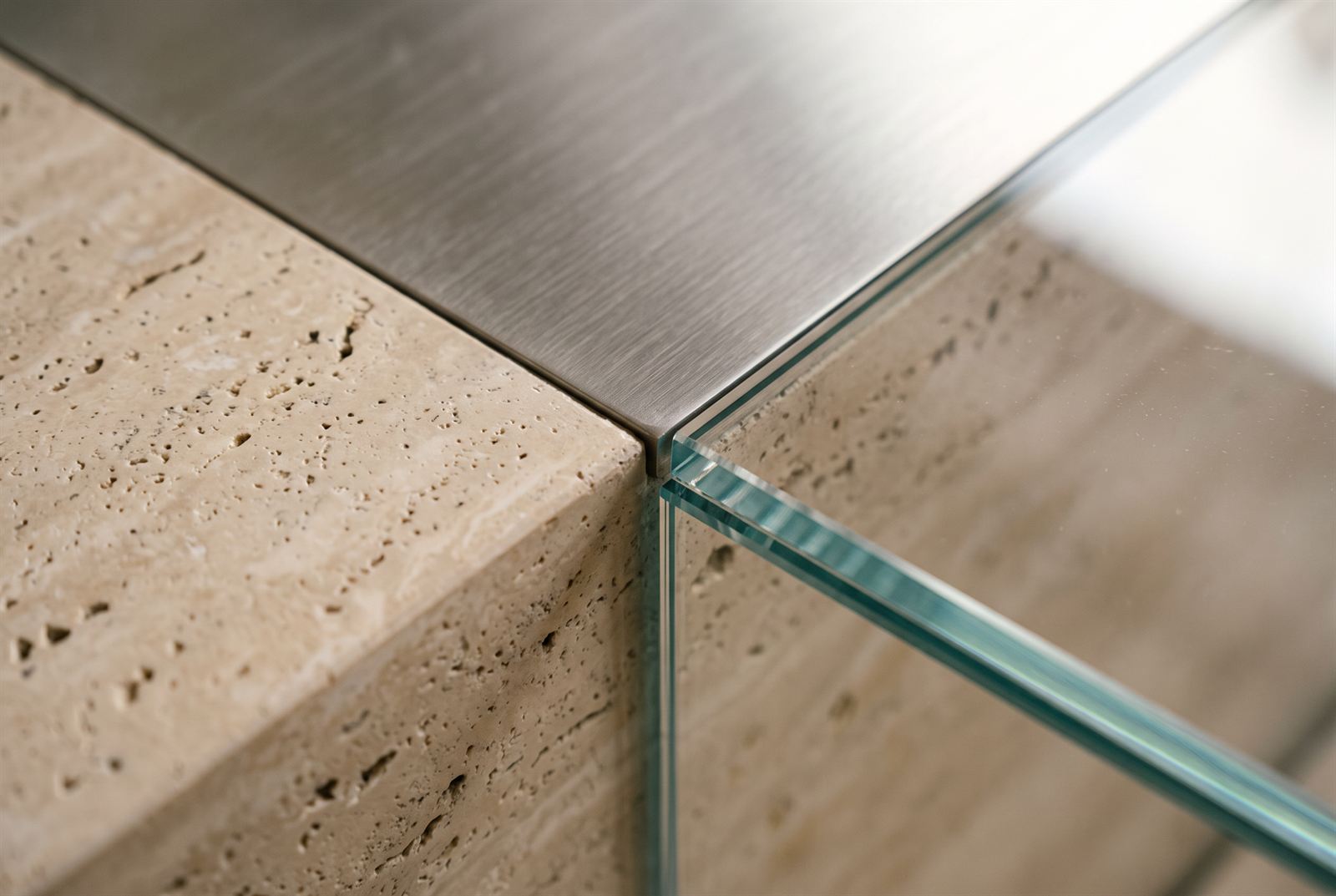 Close crop of brushed steel, low-iron glass and unfilled travertine meeting at one corner