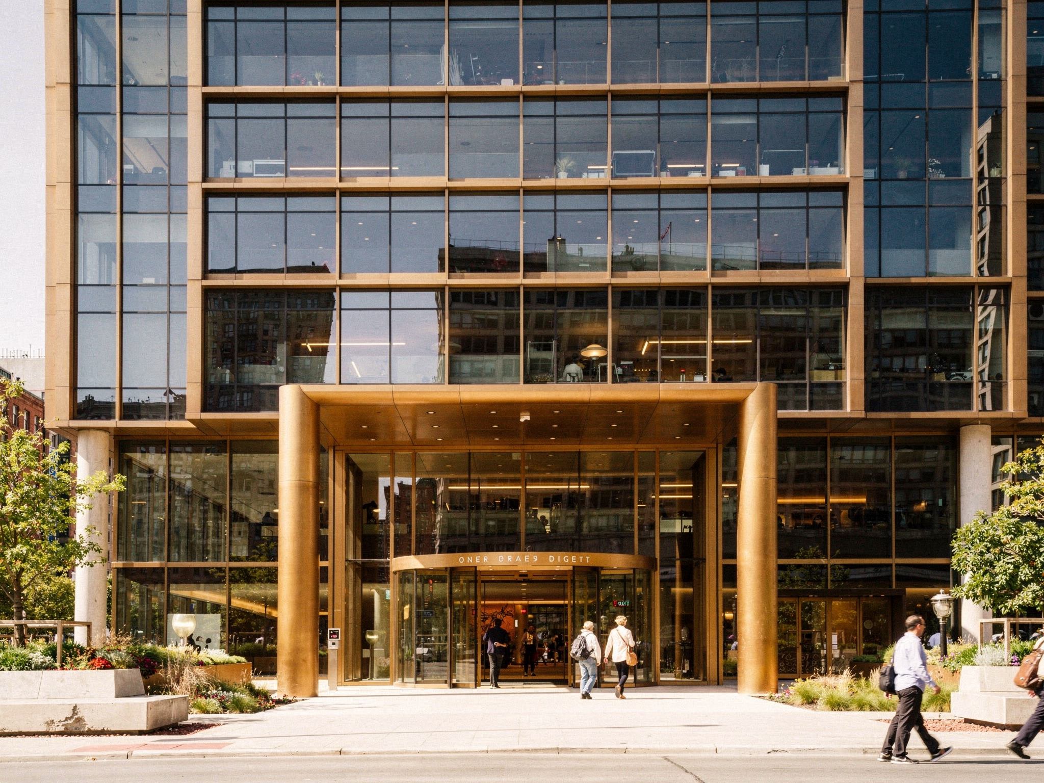 A double-height bronze-and-glass lobby entrance with people arriving