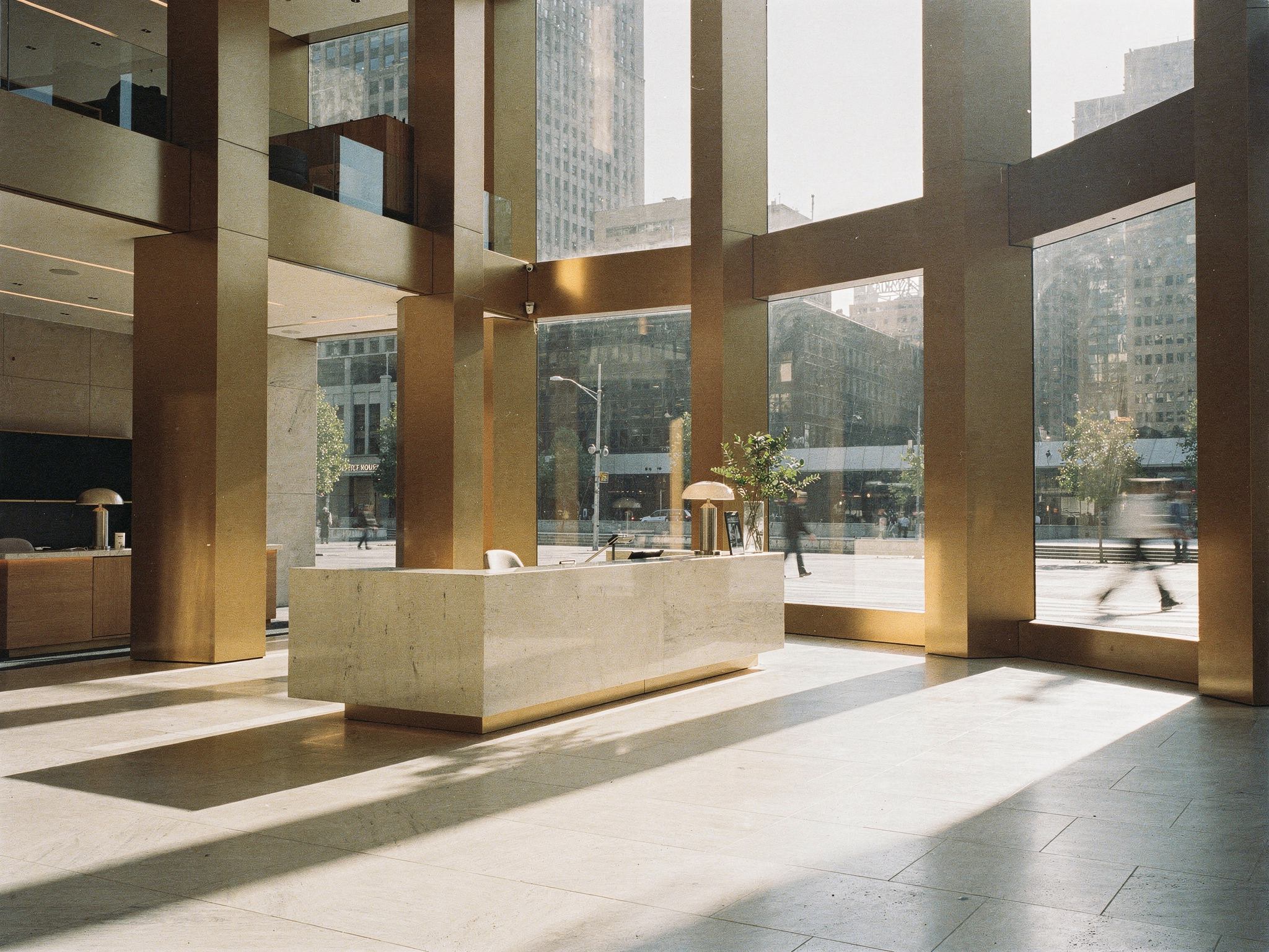 A double-height stone-and-bronze tower lobby open to the plaza
