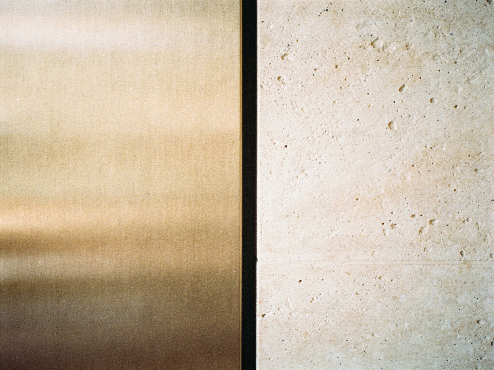 Bronze metal meeting a pale stone wall across a shadow-gap reveal