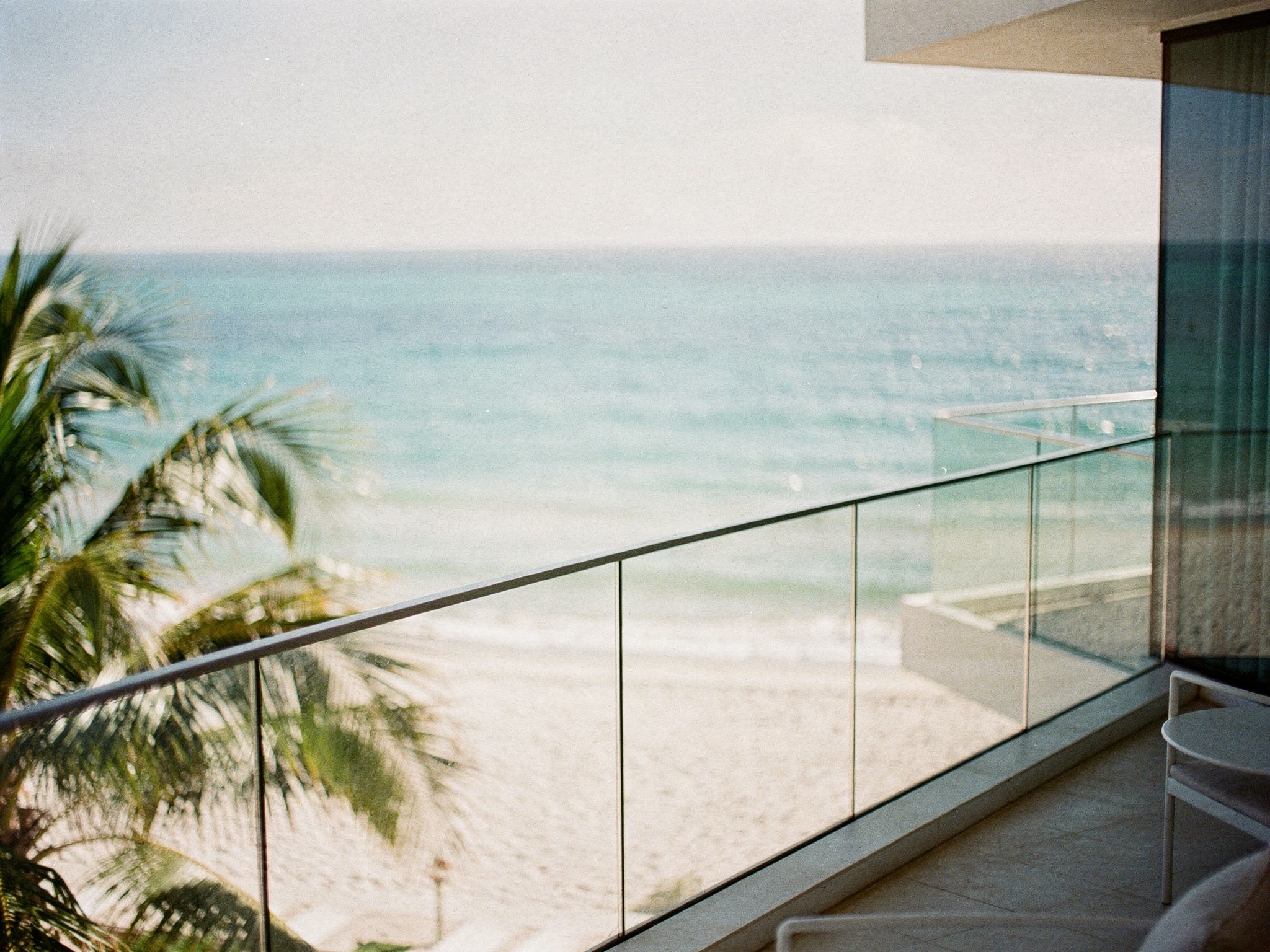 View from a suite balcony over the glass rail to the turquoise ocean and sand