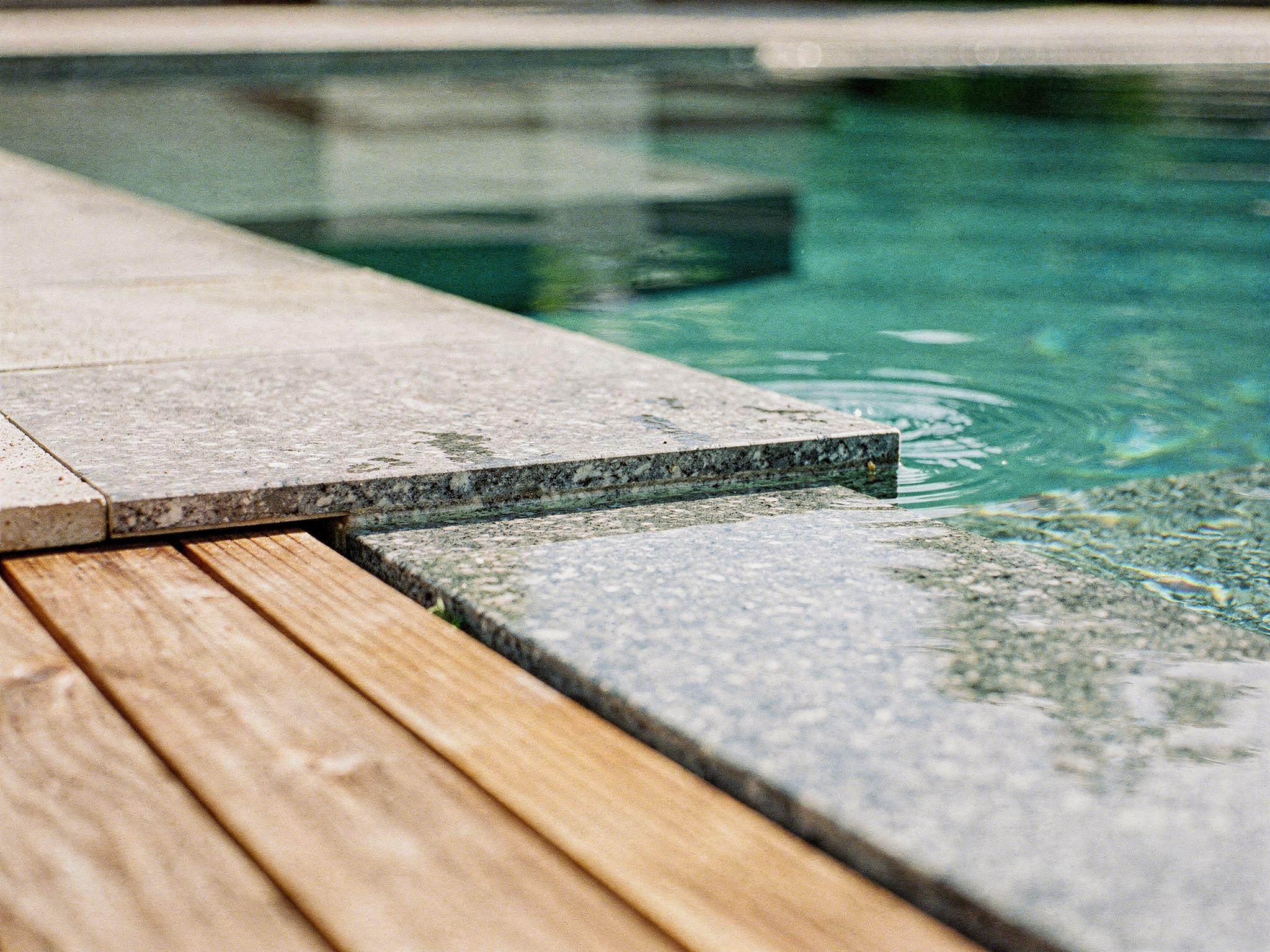 Stone pool coping meeting a teak deck at the still water