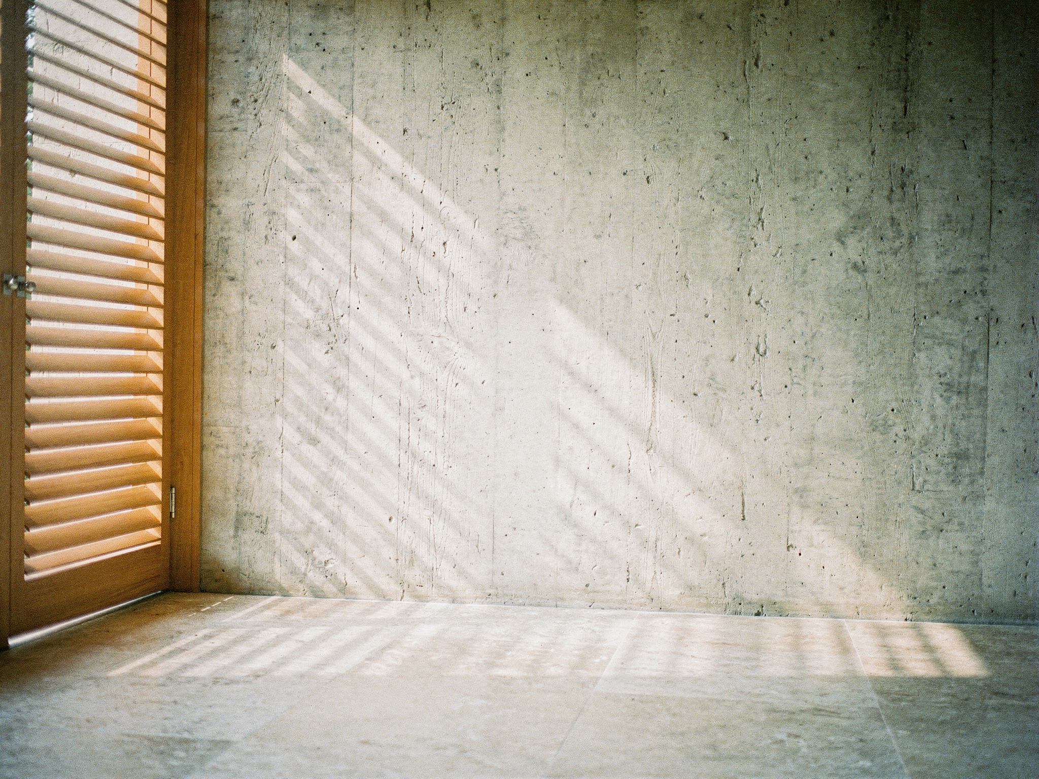 Teak louvre shadows falling across a board-marked concrete wall