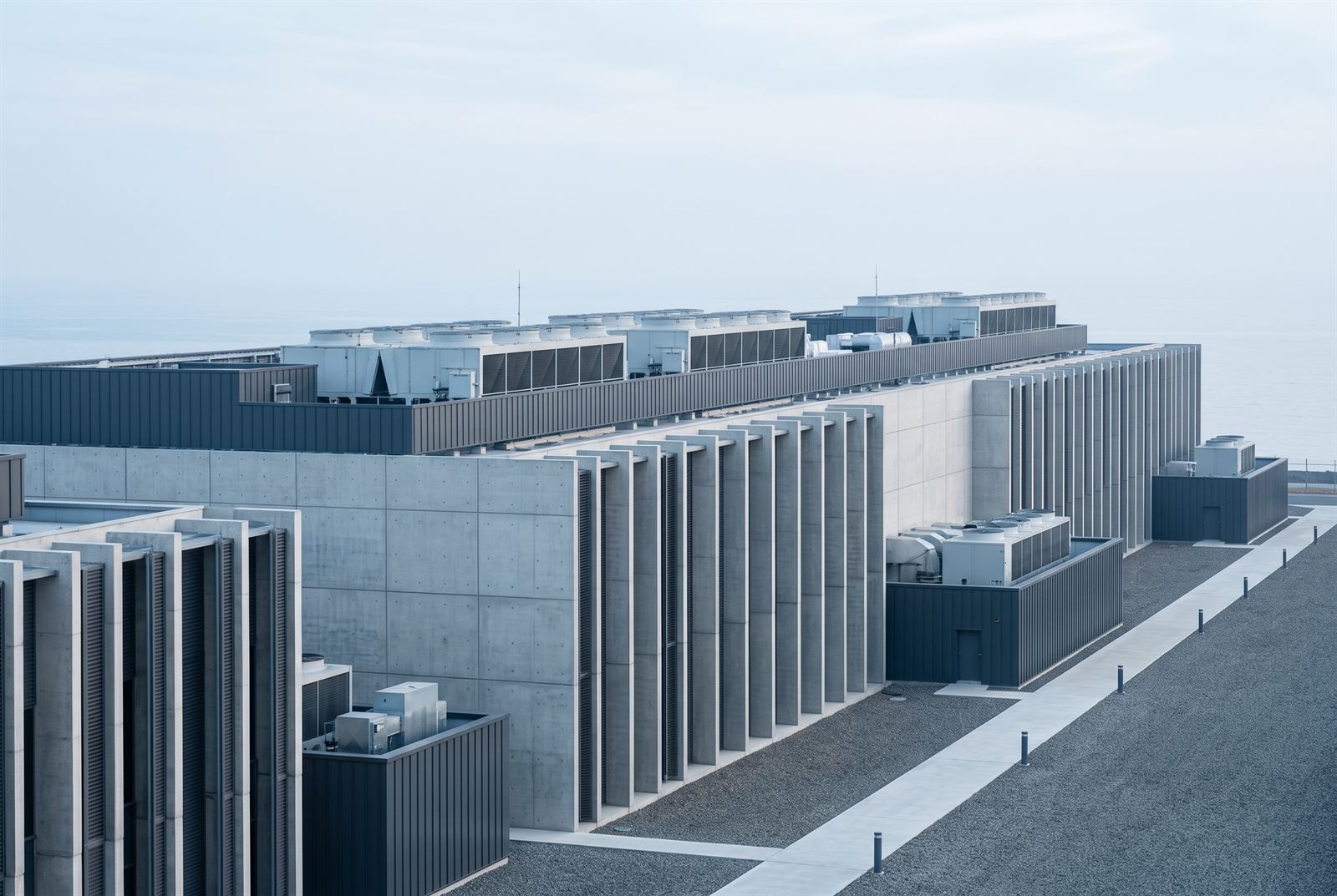 The long precast-and-zinc data hall volume with vertical concrete cooling fins and rooftop plant against a pale sea haze