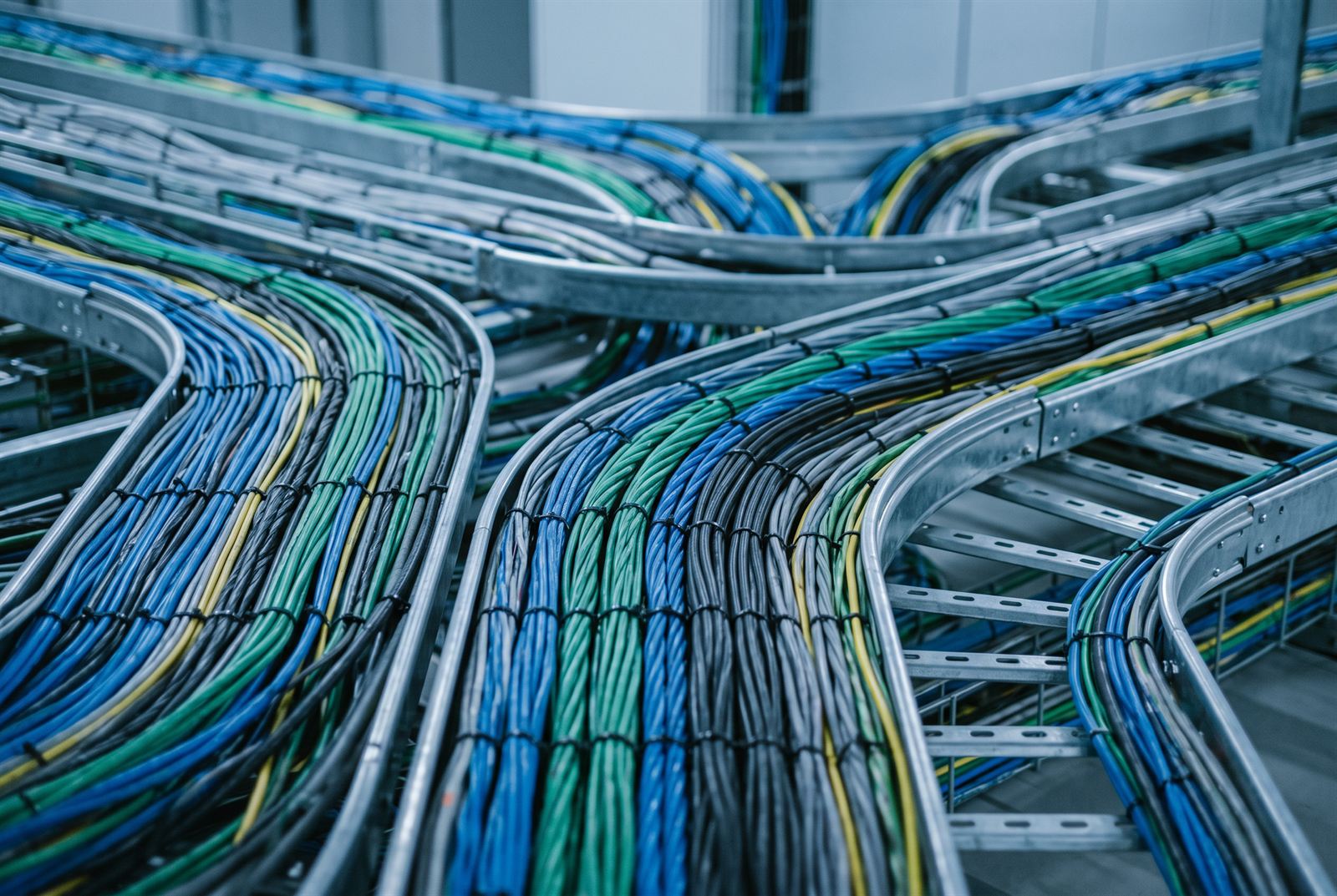 Abstract close-up of blue, green and black cable bundles curving along galvanised tray runs