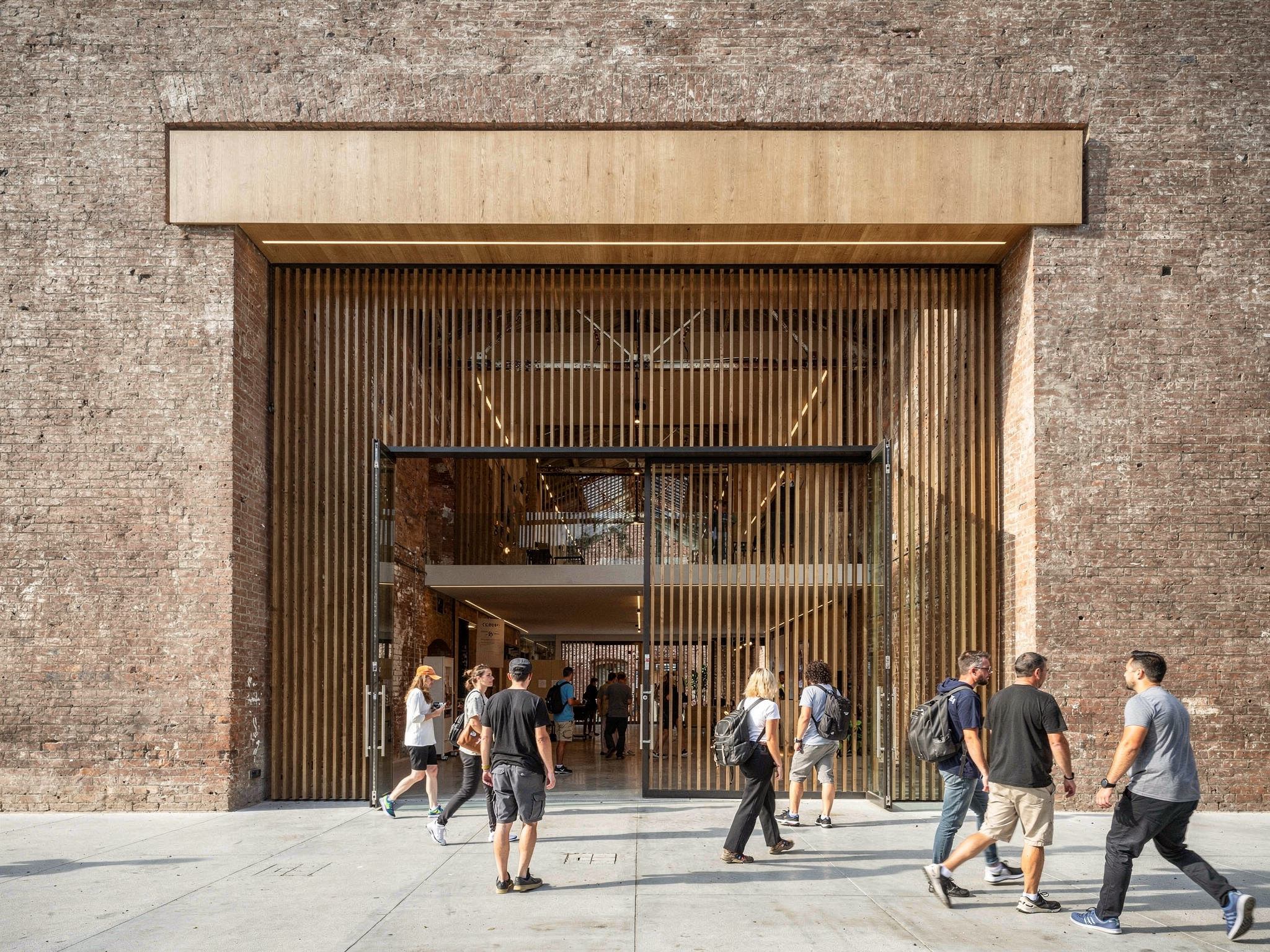 The new steel portal entrance from the street with people walking through onto the cobbles
