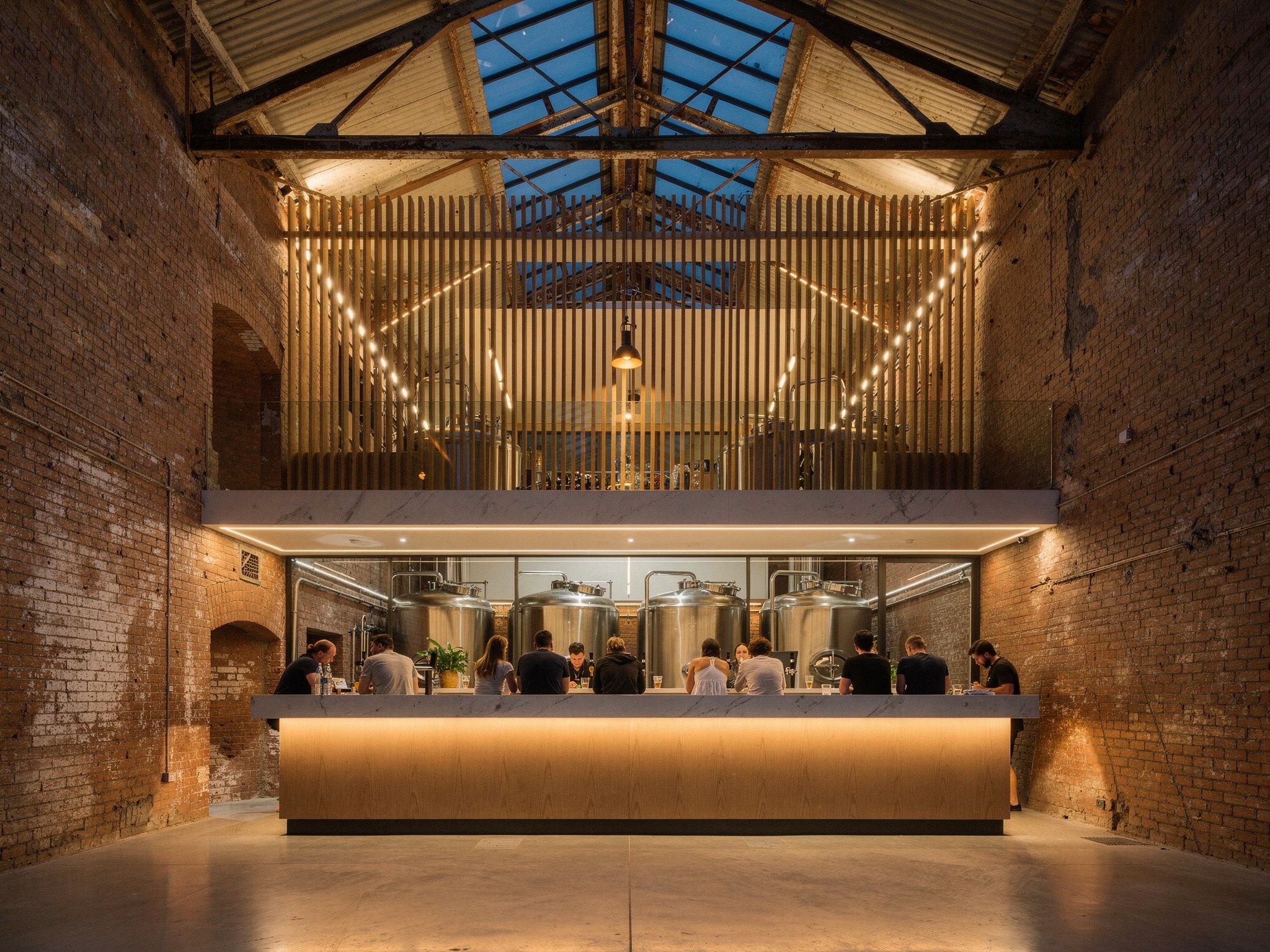 Brewery taproom with a blackened steel bar, brass taps and tanks behind glass under the old trusses