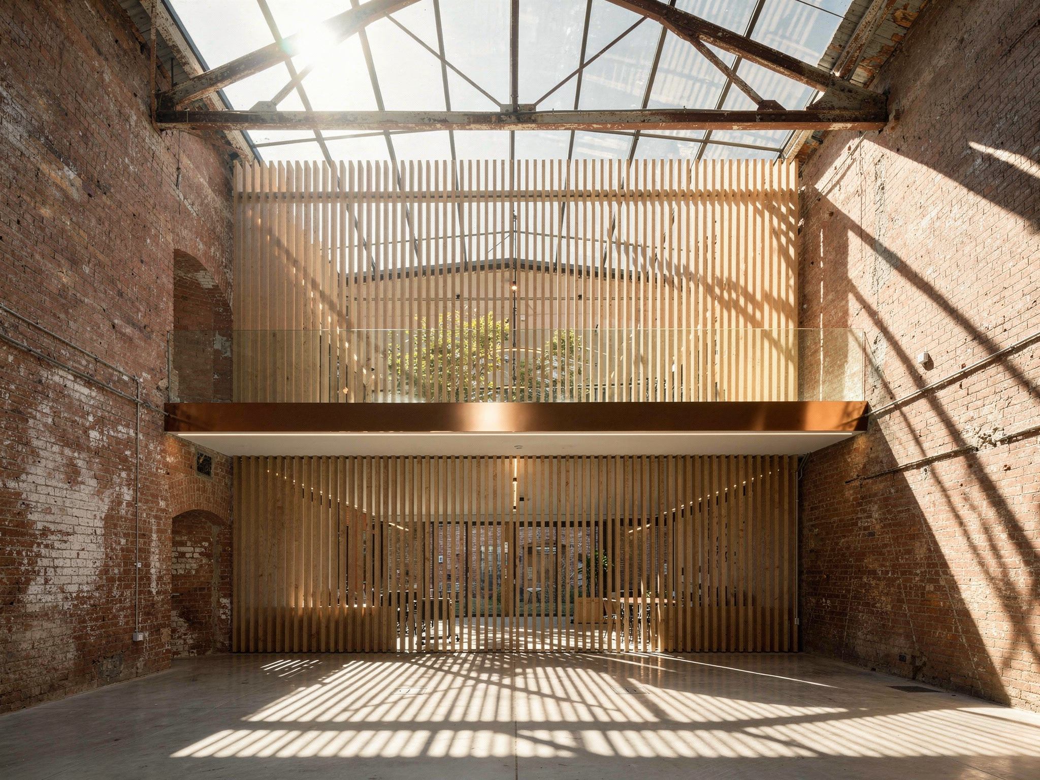 Afternoon sun through a new glazed rooflight across the brick wall and mezzanine edge