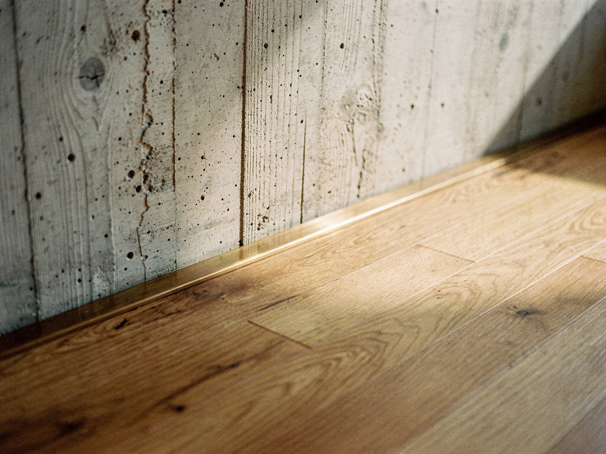 Board-formed concrete wall meeting oak floor across a brass reveal