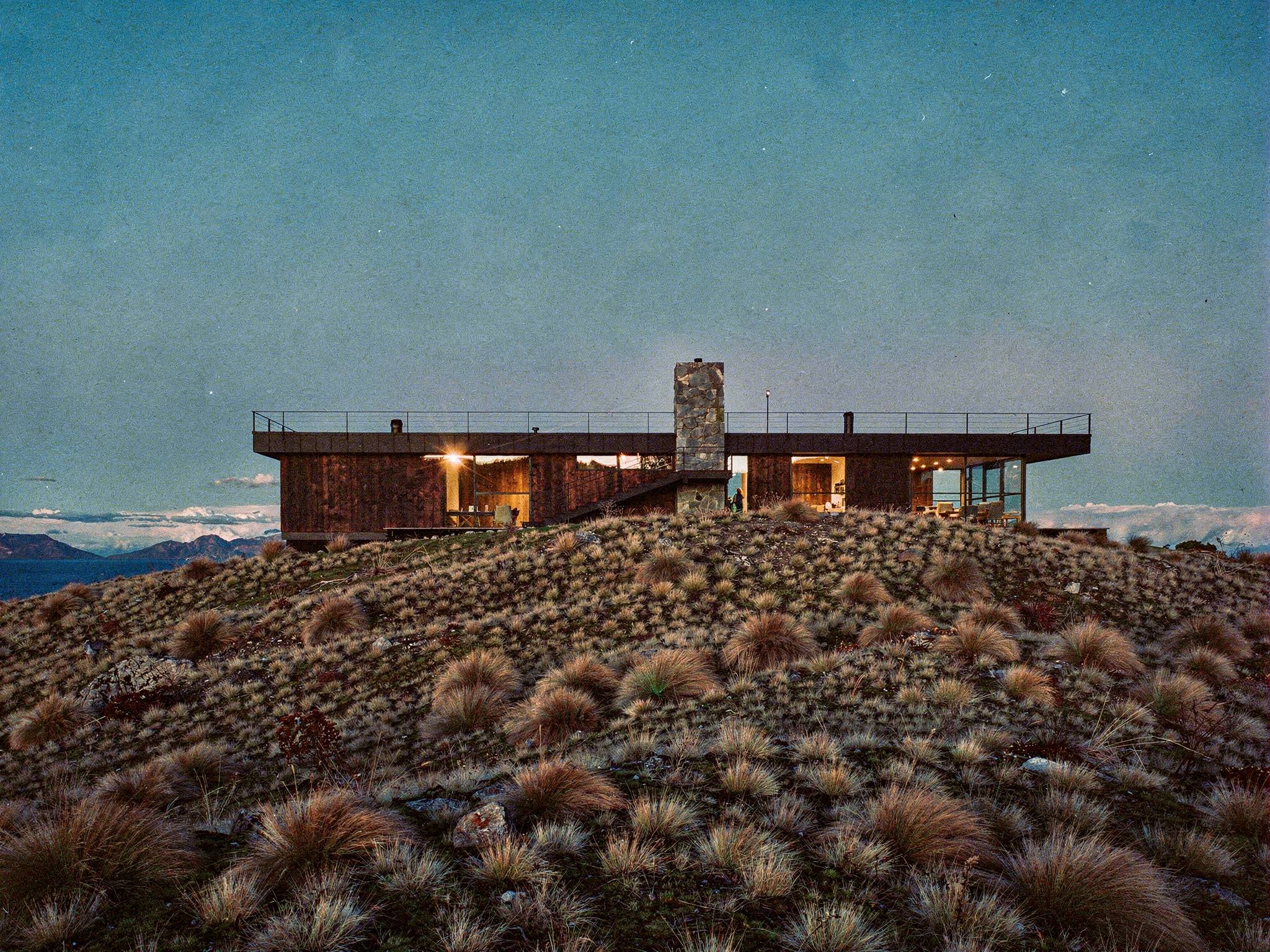 Wānaka Ridge House at nightfall, interiors warm above the lake